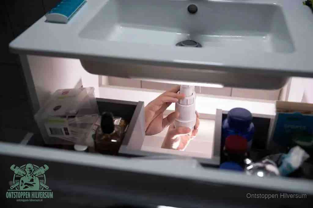 Een pompfles met zeep boven een wastafel, de heet water en afwasmiddel-methode om een vetprop in de afvoer los te maken in Hilversum