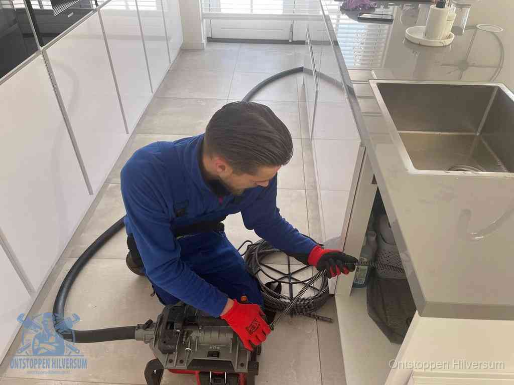 Een monteur ontstopt de keukenafvoer onder de spoelbak met een elektrische veermachine in Hilversum