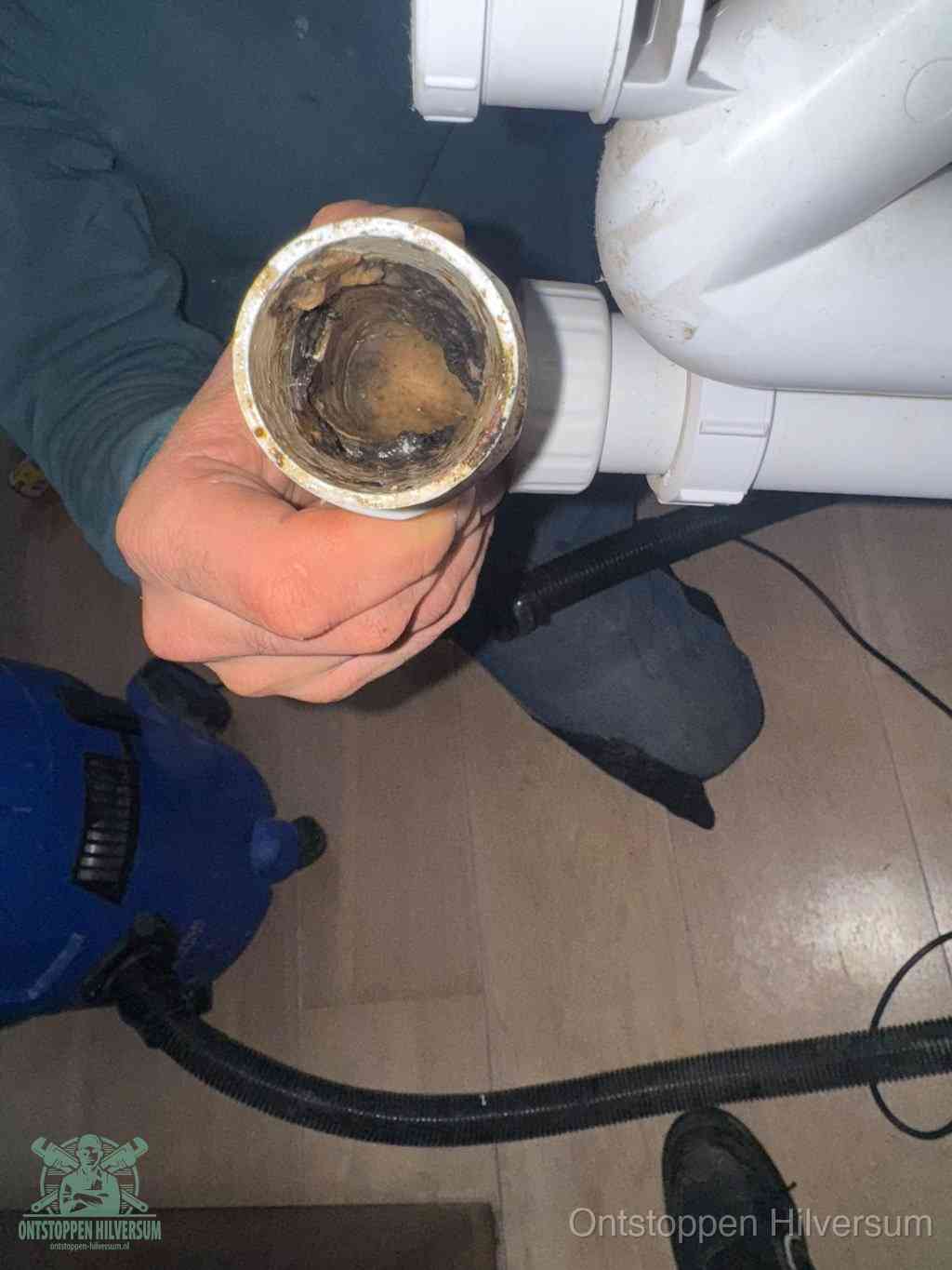 Een hand houdt een losgekoppeld PVC-afvoerbuisstuk vast dat van binnen volledig is dichtgeslibd met vet, vuil en aanslag, de meest voorkomende oorzaak van een verstopte afvoer in Hilversum