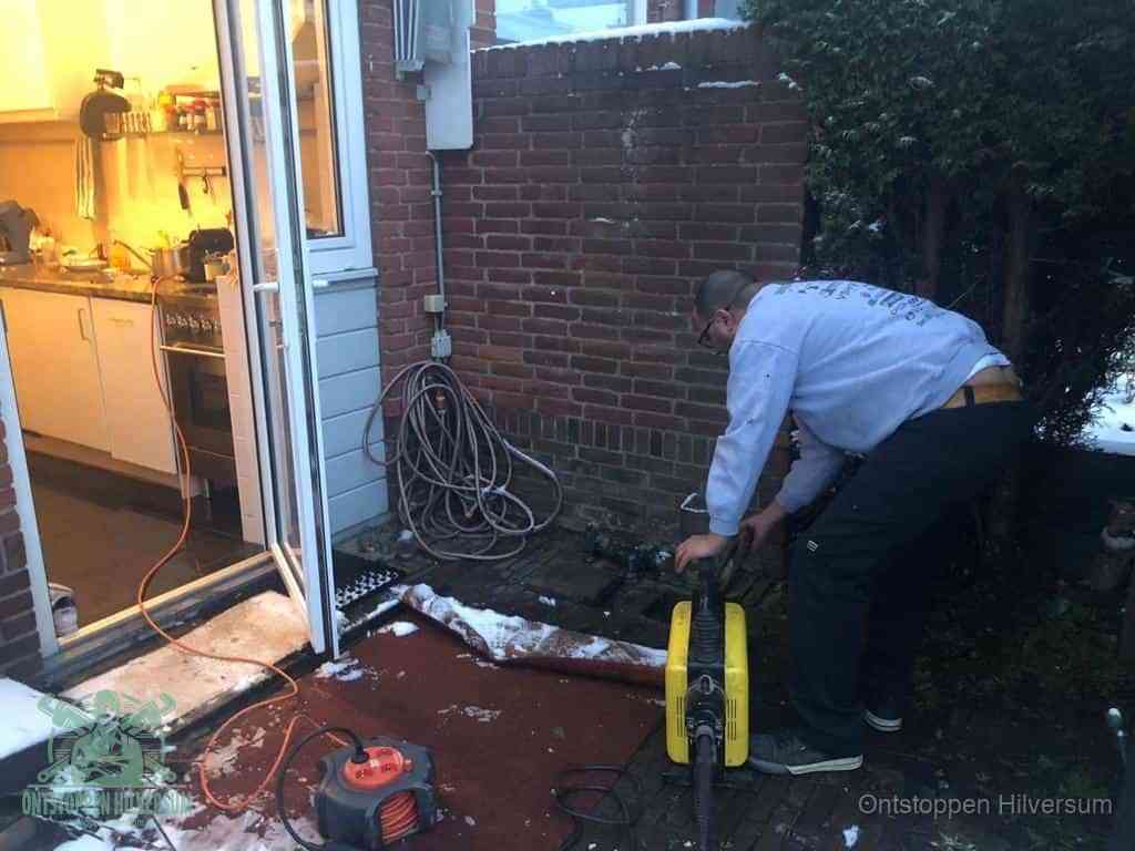 Een monteur werkt buiten bij een open riool-/grondput met een elektrische ontstoppingsmachine om een verborgen afvoerprobleem op te sporen in Hilversum