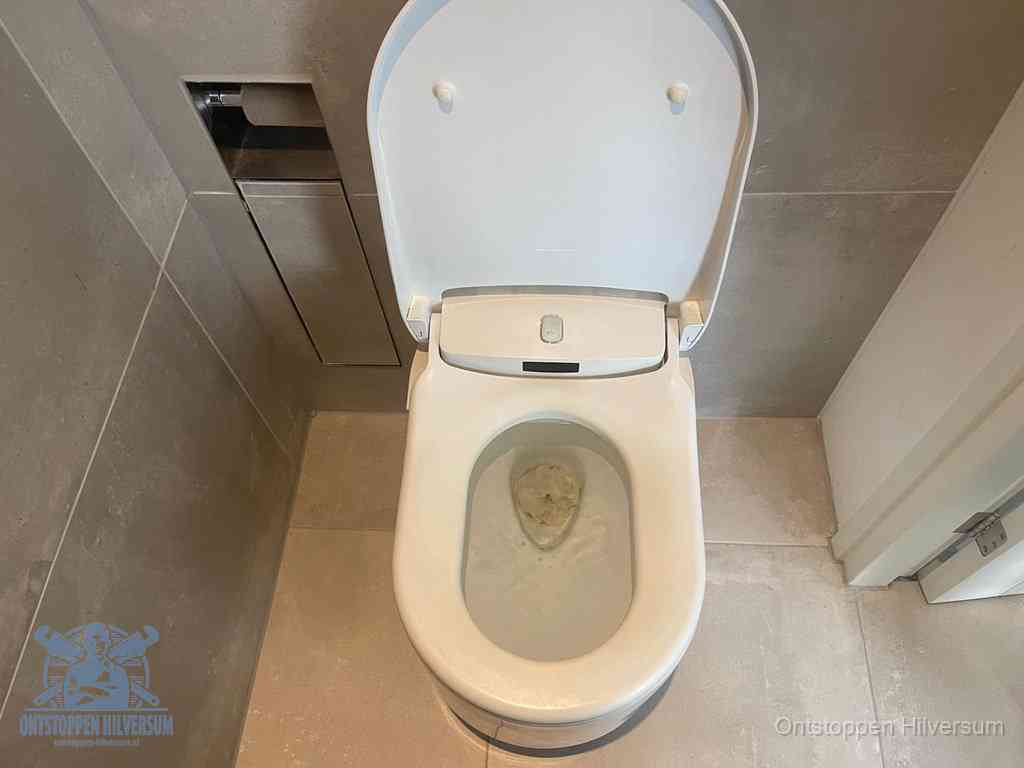 Een wit hangtoilet waarin een prop wc-papier op het water blijft drijven, een duidelijk signaal van een verstopte wc in Hilversum