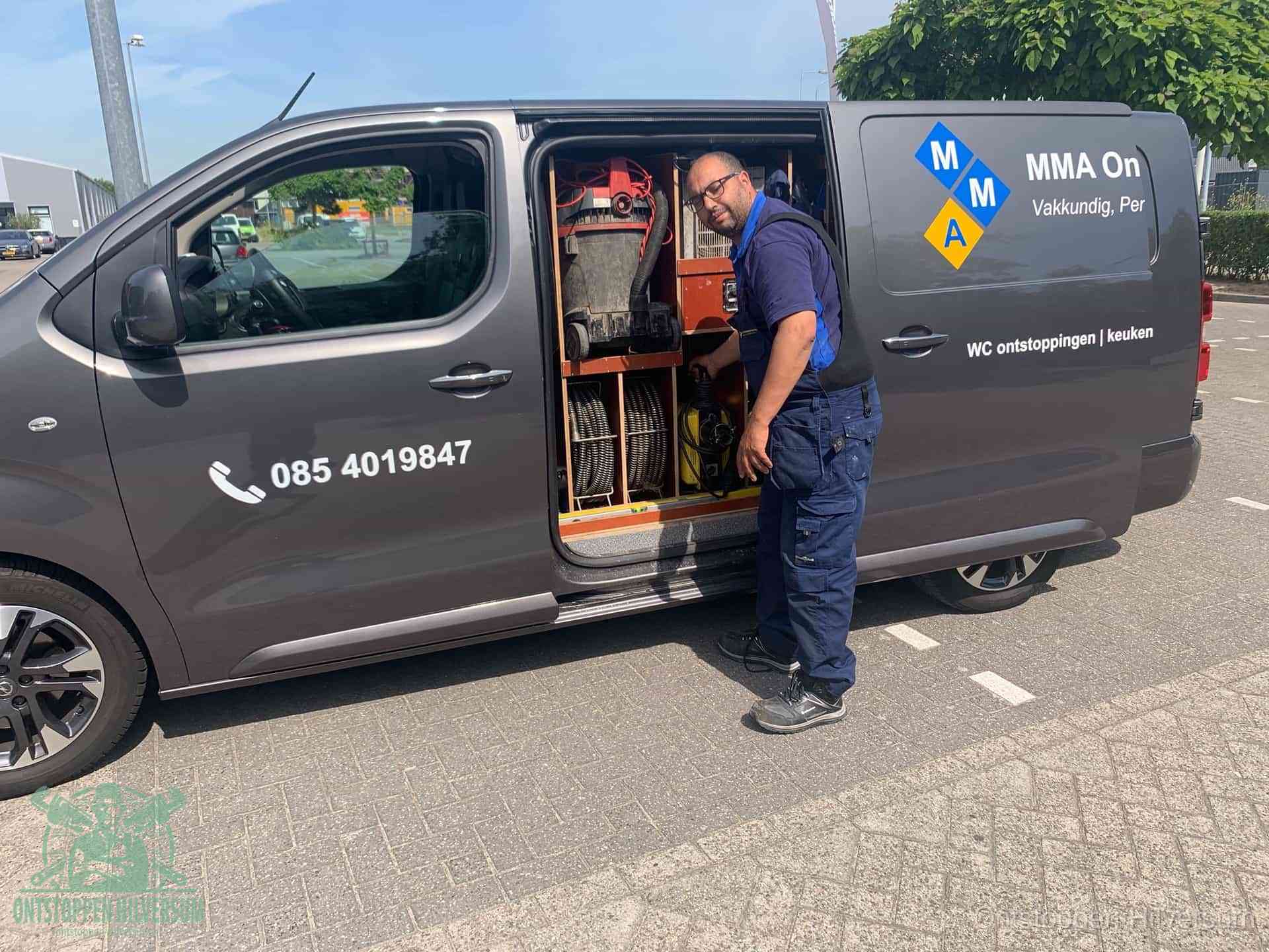Een monteur bij de open schuifdeur van zijn bedrijfsbus op een parkeerplaats, klaar om de oorzaak van terugkerende afvoerverstoppingen aan te pakken in Hilversum