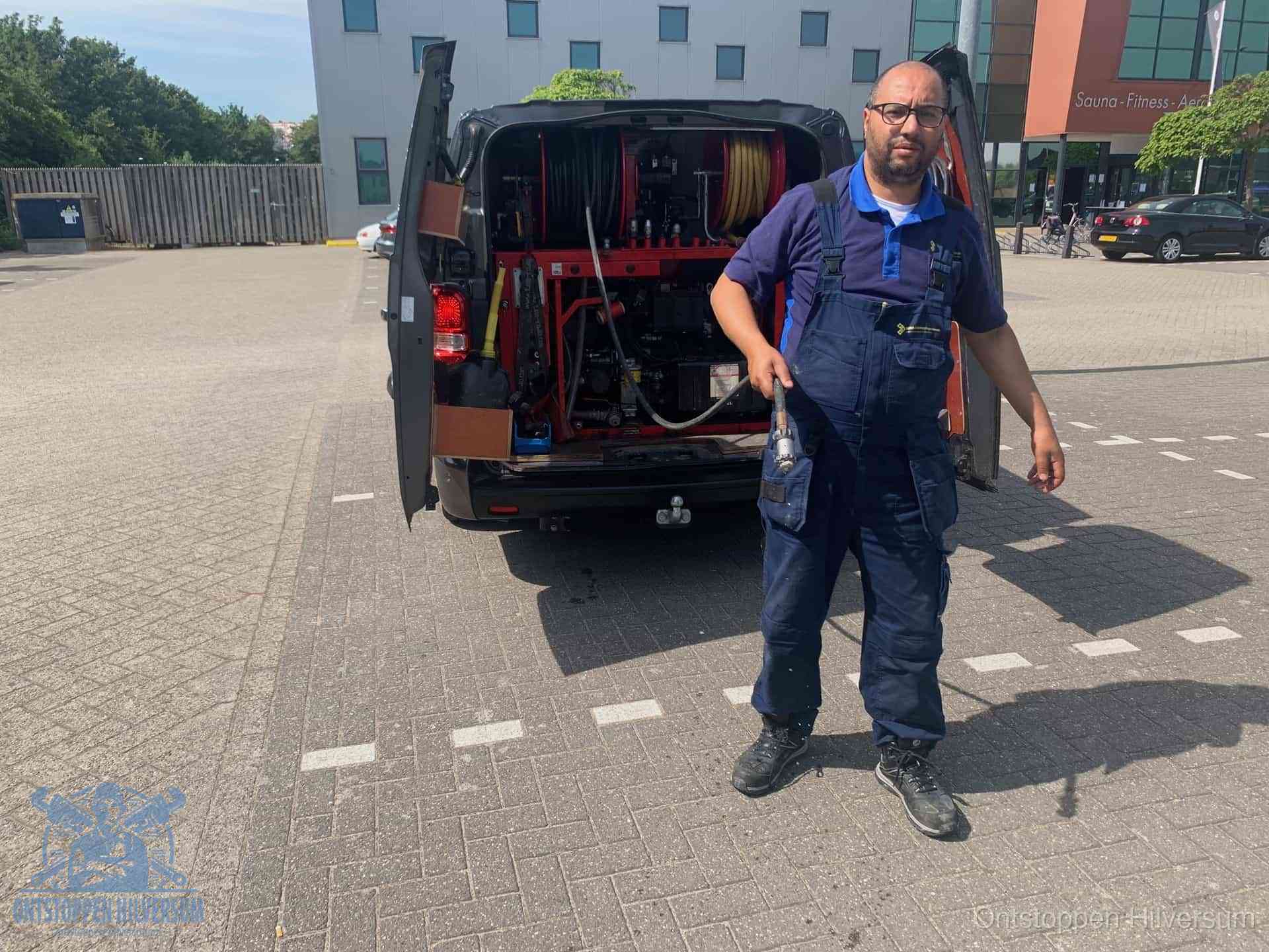 Een monteur bij zijn bestelbus met een hogedruk- en rioolreinigingsunit, klaar om de oorzaak van terugkerende wc-verstoppingen aan te pakken in Hilversum