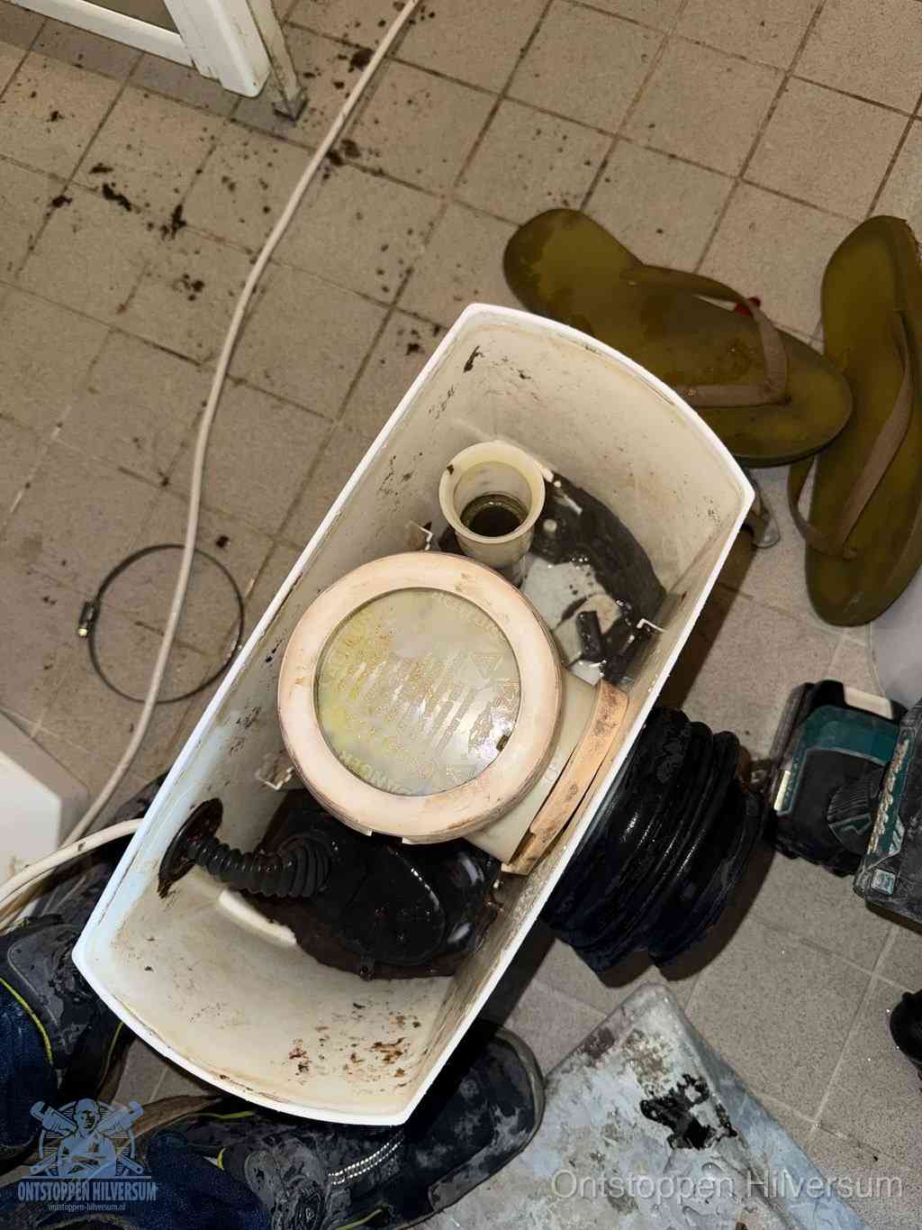 Een gedemonteerde toiletpot op de vloer met ontstoppingsveer en gereedschap ernaast, het verwijderen van een vastzittend voorwerp uit de wc in Hilversum